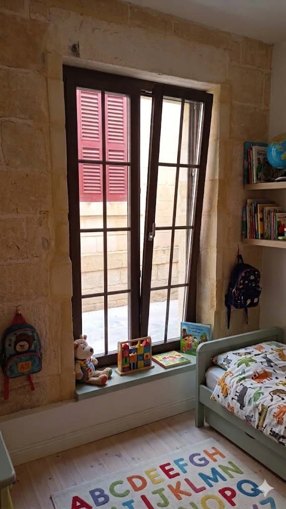Dark timber bedroom window with slim glazing bars set into a Maltese stone wall